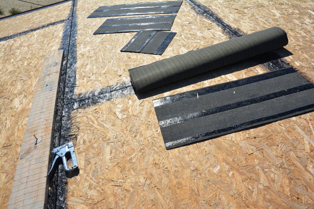 A plywood roof deck with a roll of roofing felt, several cut strips of underlayment, and a staple gun.
