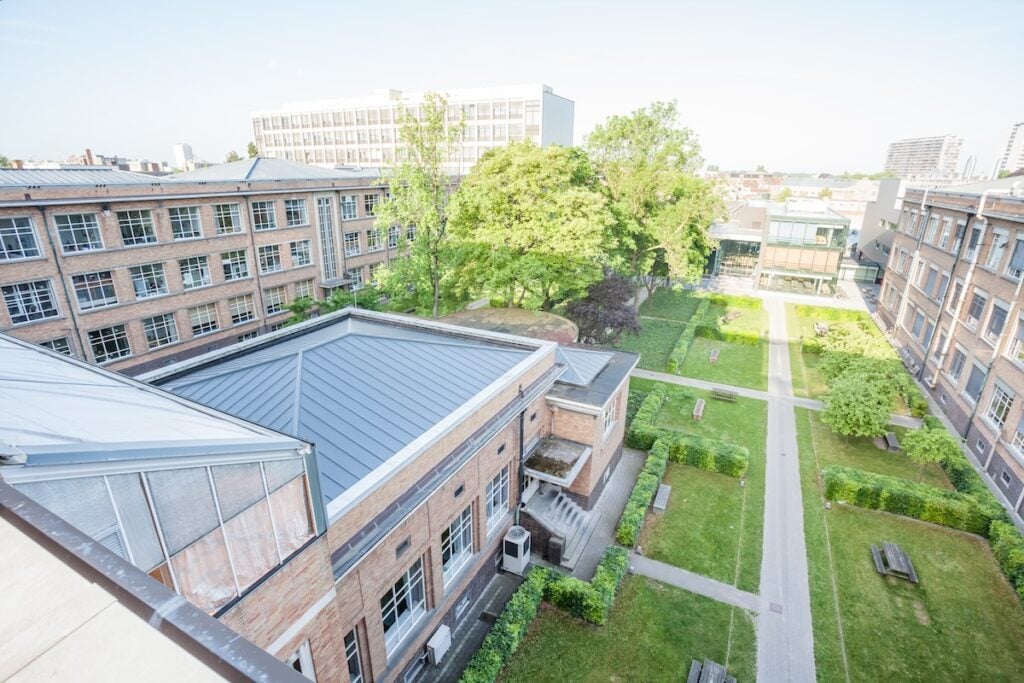 apex nc commercial Aerial view of a campus courtyard. It features pathways, green lawns, and benches. Surrounded by brick academic buildings with distinctive roofing and lush trees reminiscent of a serene forest. A larger building is visible in the background under a clear blue sky.