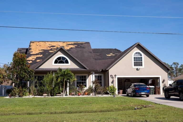 A suburban house shows signs of storm damage, with missing shingles on the roof