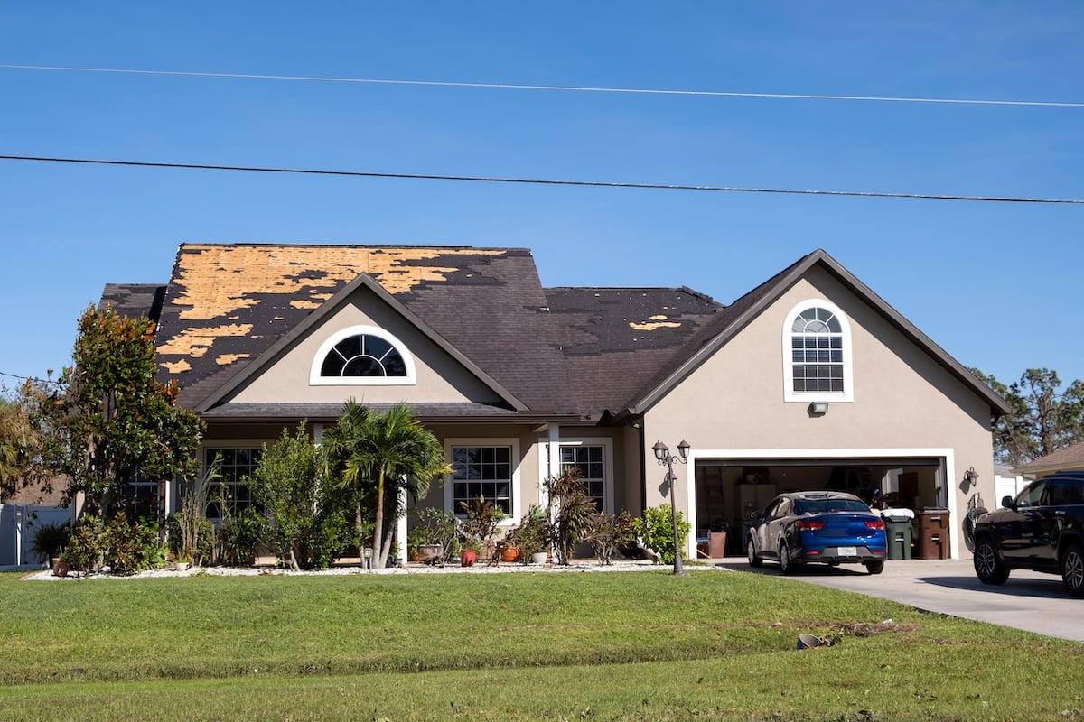 A suburban house shows signs of storm damage, with missing shingles on the roof