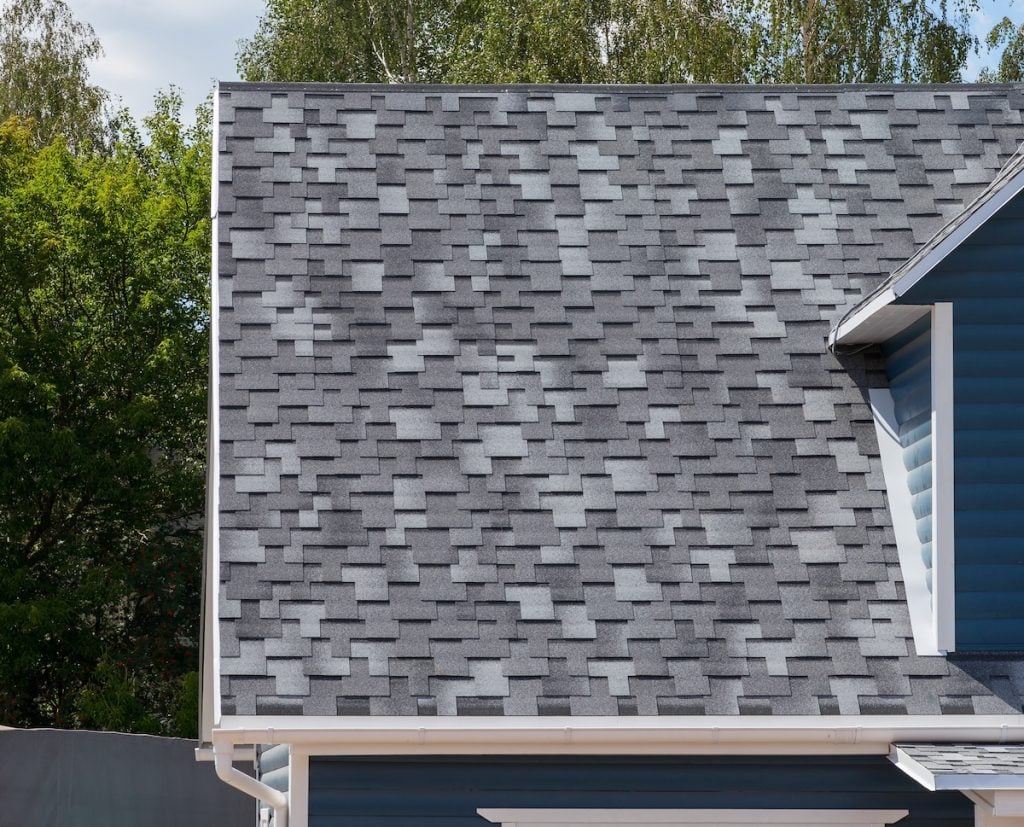 Close-up view of a house roof with gray asphalt shingles in a staggered pattern