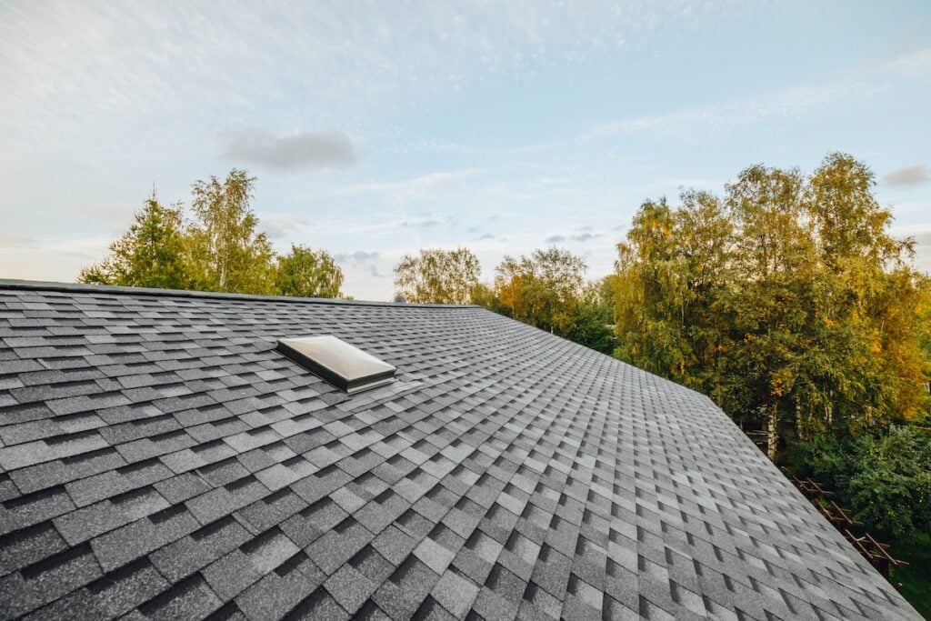 A sloped roof covered with gray asphalt shingles, featuring a single skylight.