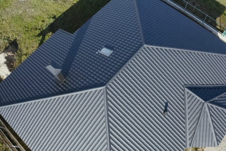 Aerial view of a modern house roof with dark-colored metal panels and metal roof coating