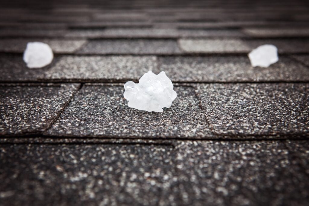 Close-up of three pieces of hail on a textured shingle roof.