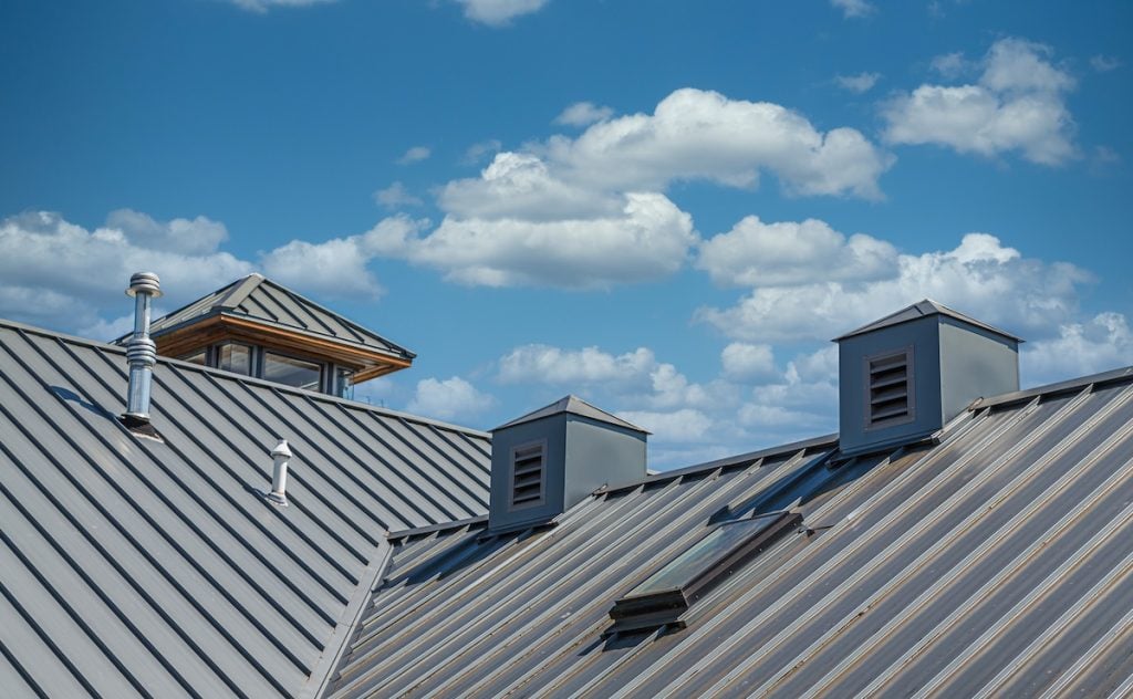 A close-up view of a metal roof featuring two vented cupolas and a small skylight, showcasing metal roofing innovations