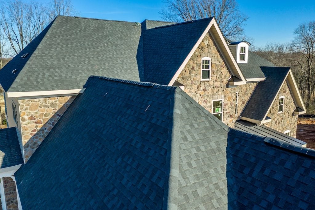 Aerial view of a house with stone exterior walls and shingle roof with ridge vent