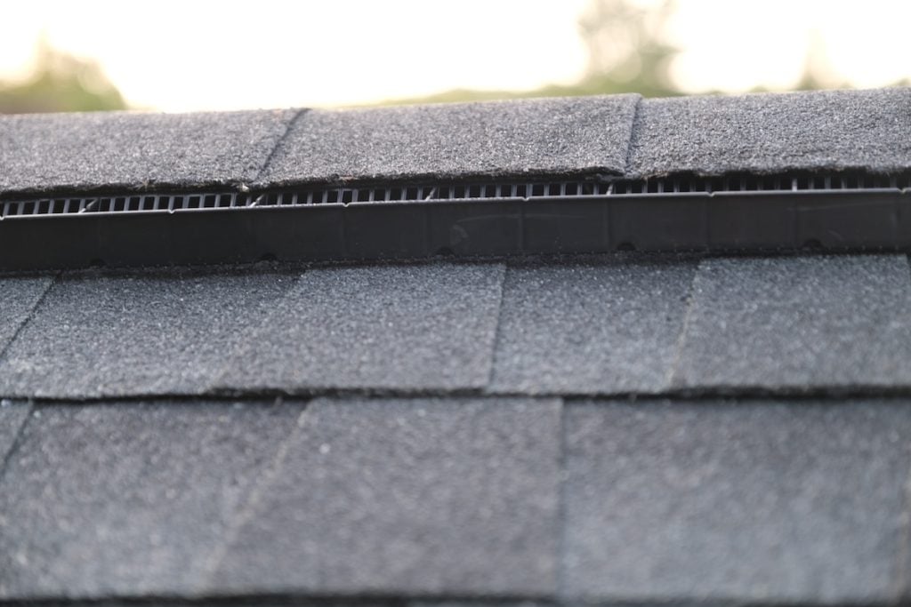Close-up of dark asphalt roof shingles with a visible ridge vent along the roofline, which aids attic ventilation.