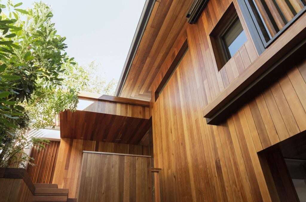 A modern house exterior featuring rich, warm wood paneling as a type of siding under a clear sky