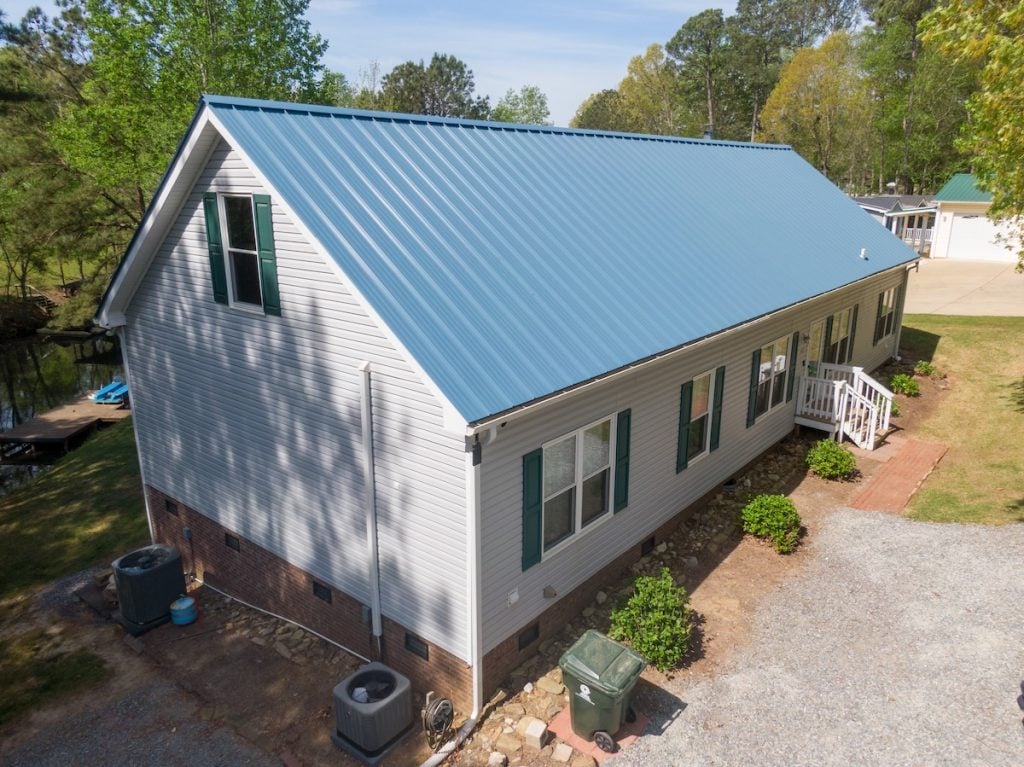 Aerial view of a house with a blue metal roof, white siding, and green shutters.