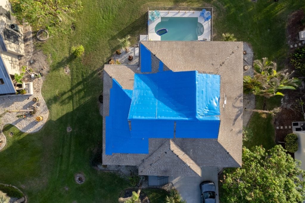 Aerial view of a house with an emergency roof tarp covering parts of its roof, likely for protection or repair.