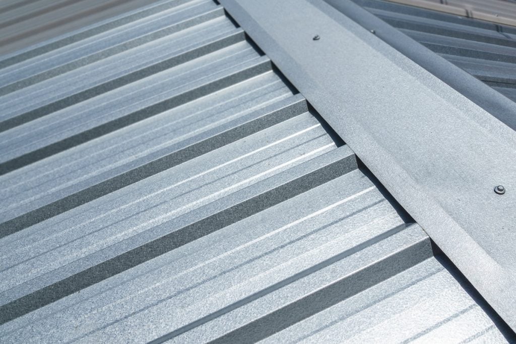 Close-up view of a silver metal roof with overlapping corrugated panels and a central ridge cap