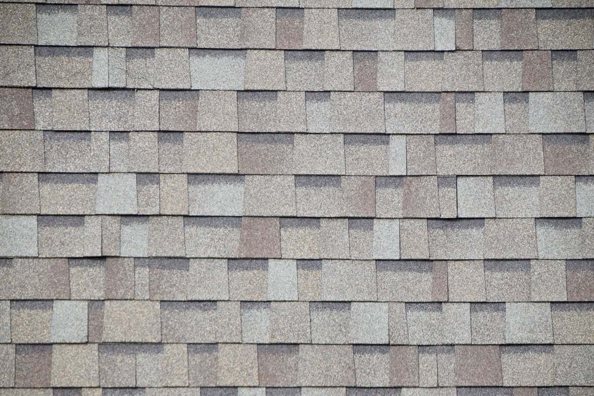 Close-up view of a roof with overlapping rectangular dimensional shingles in various shades of gray and brown, arranged in a staggered pattern.