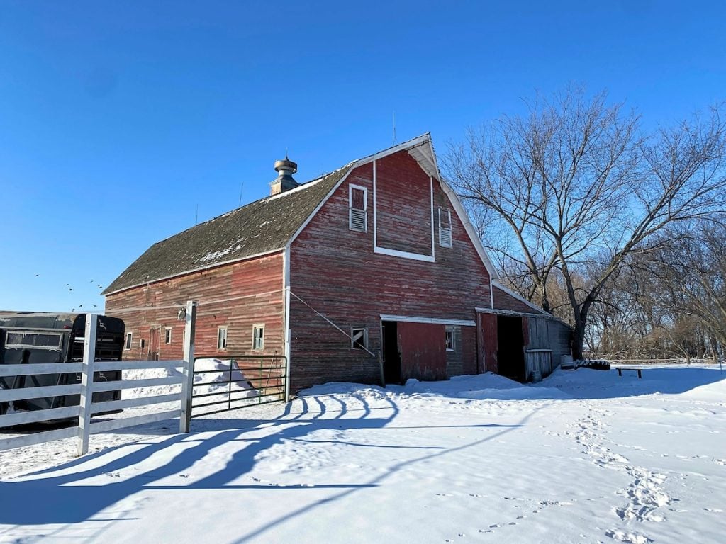 A red wooden barn with a damaged gambrel roof