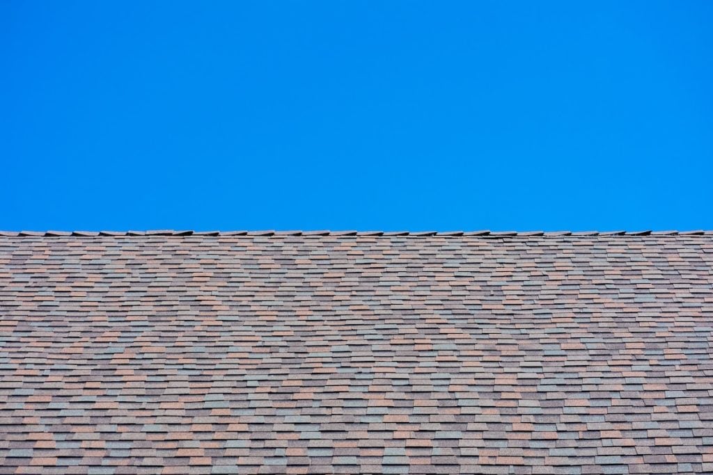 A close-up view of a roof covered with multi-colored dimensional shingles, set against a clear blue sky in the background