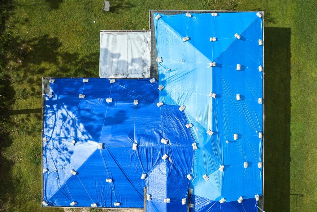 Top view of leaking house roof covered with protective tarp sheets against rain water leaks until replacement of asphalt shingles