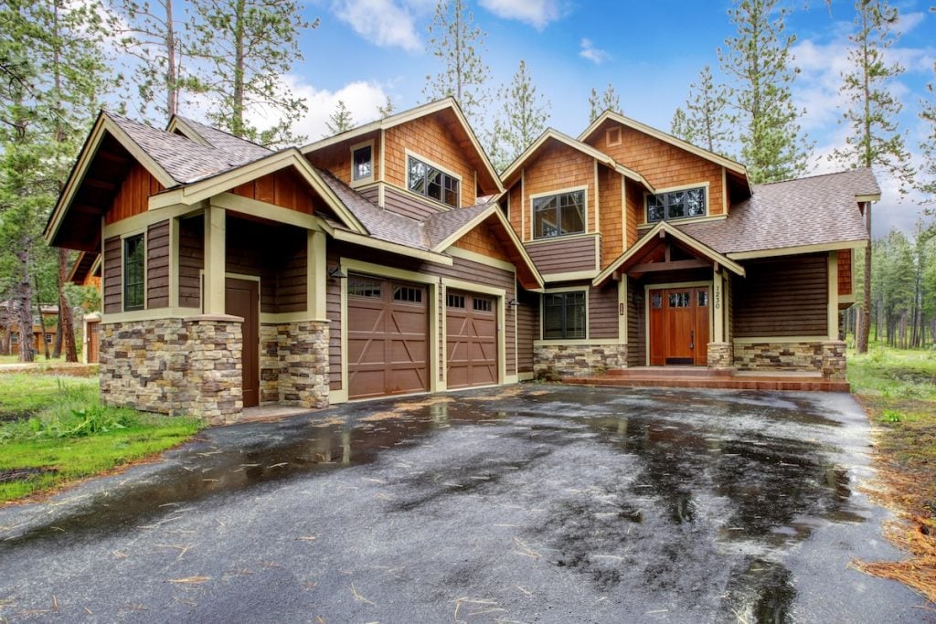 Large cabin house with stone and driveway after rain.