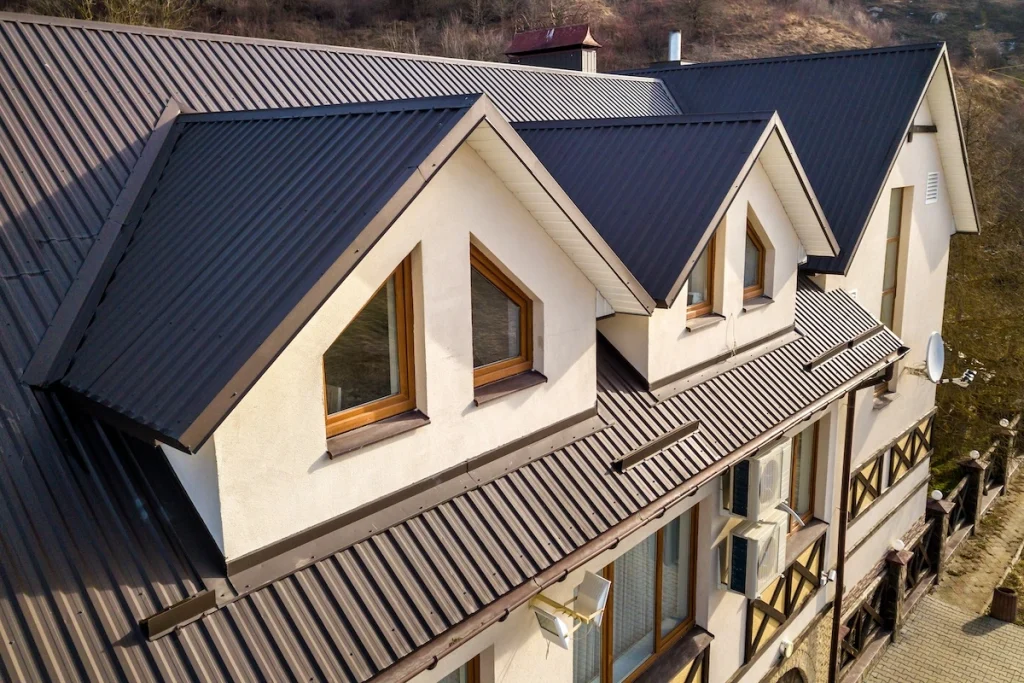 A beige house with a dark metal roof and three triangular dormer windows, seen from above.