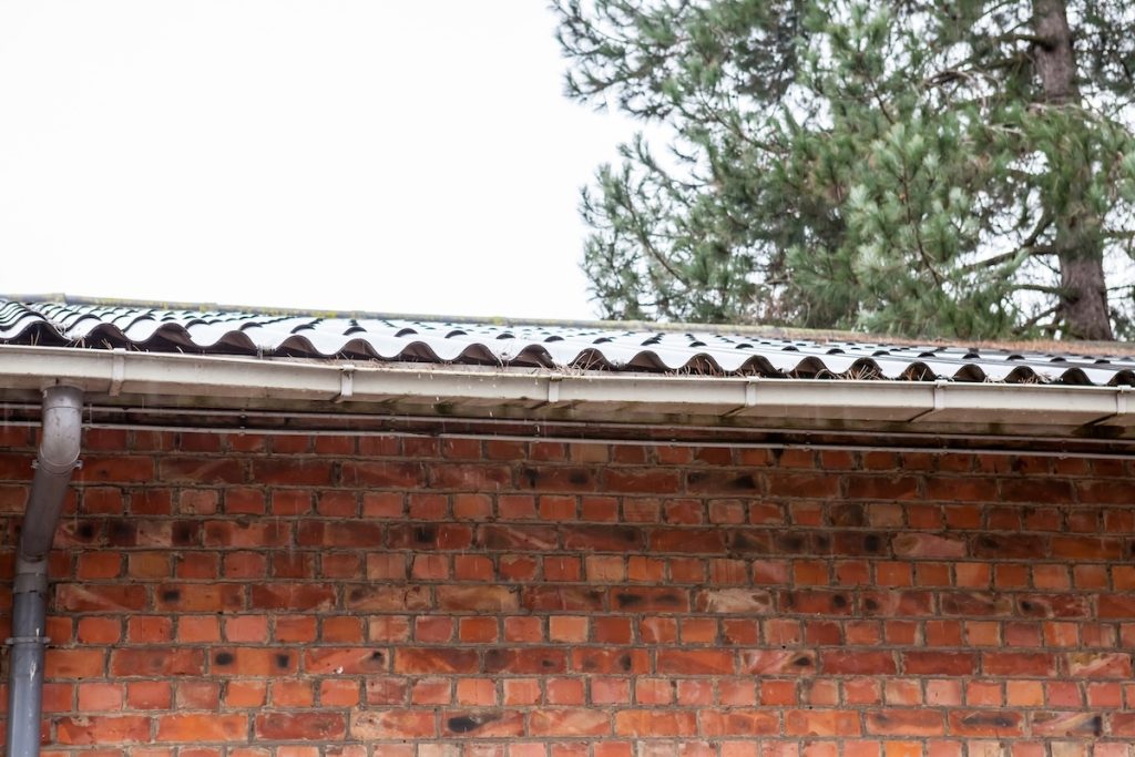 A brick building with a corrugated metal roof and a rain gutter, sagging