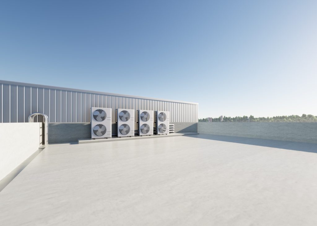 A rooftop with several large industrial air conditioning units lined up against a metal wall, under a clear blue sky. The smooth, expansive roof hints at the scale involved—raising questions like how much does a commercial roof inspection cost.