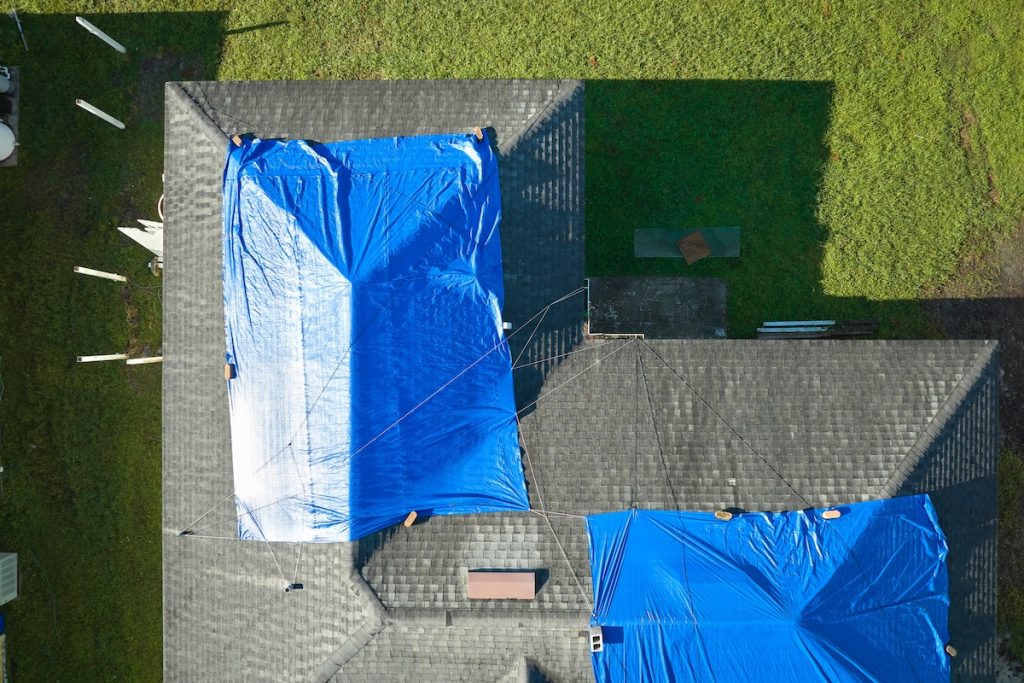 Top view of leaking house roof covered with protective tarp sheets against rain water leaks until replacement of asphalt shingles. Damage of building rooftop as aftermath of storm