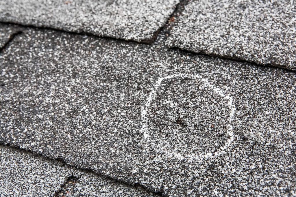 Close-up of gray asphalt roof shingles with a white chalk circle marking a damaged area,