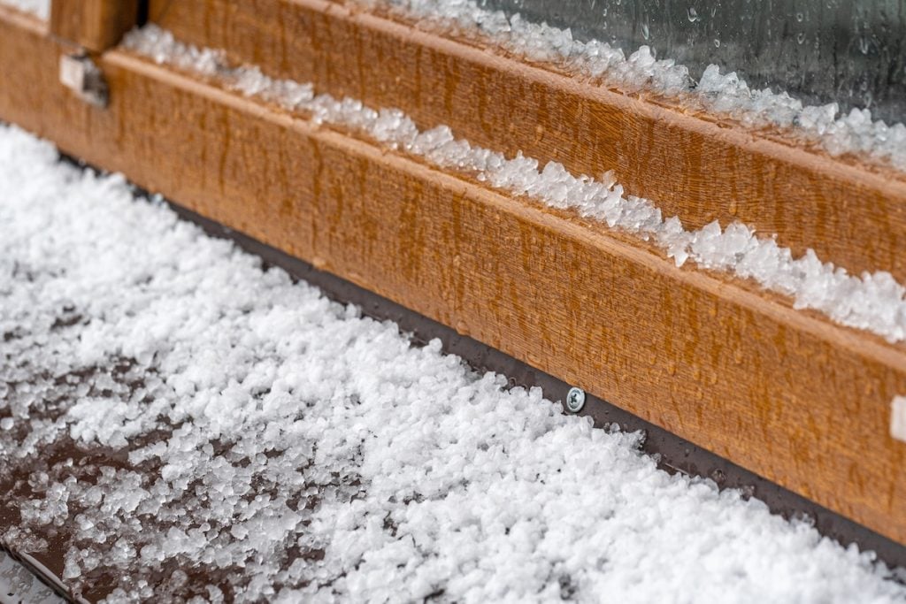 Small white hailstones cover a brown roof