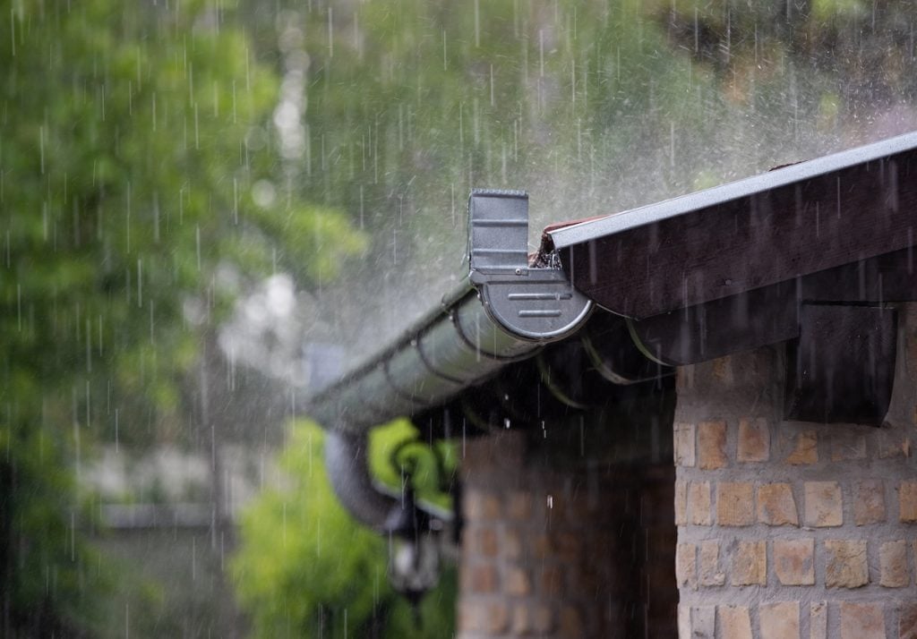 Heavy rain falling on the roof and metal gutter of brick house in summer season