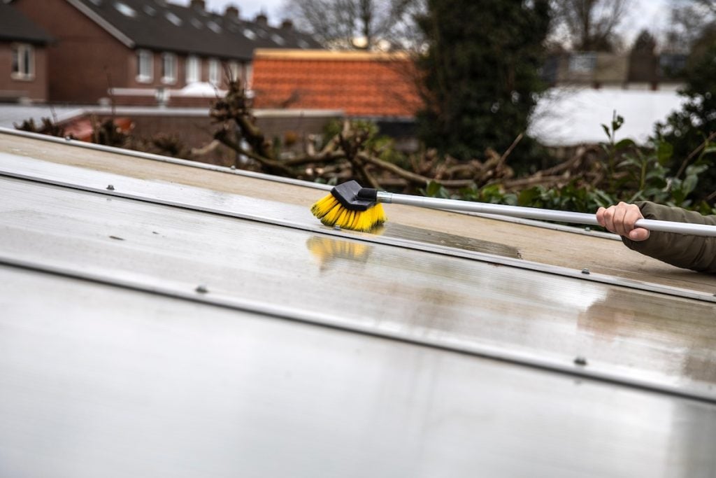 A person uses a yellow-bristled brush with a long handle, one of the top roof cleaning products