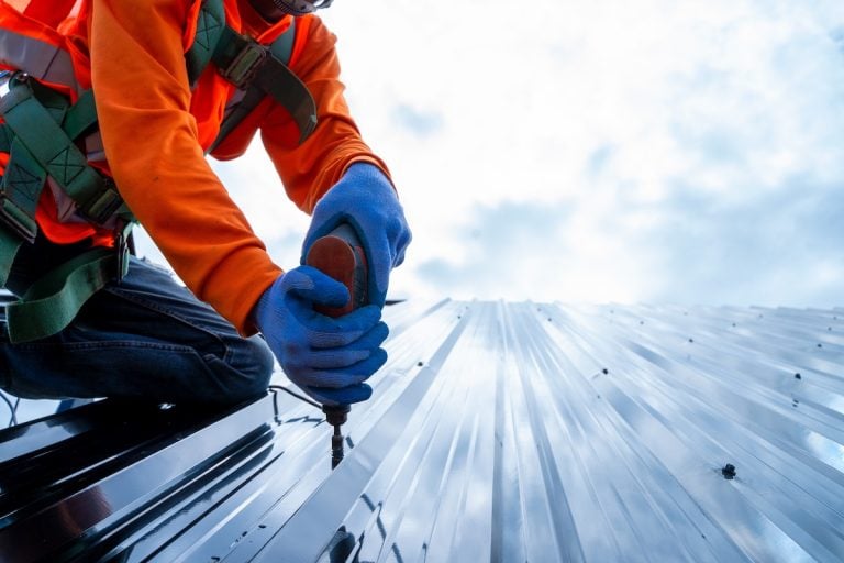 Close up photo of Professional and qualified roofer in protective uniform wear use electric drill to install the metal sheet