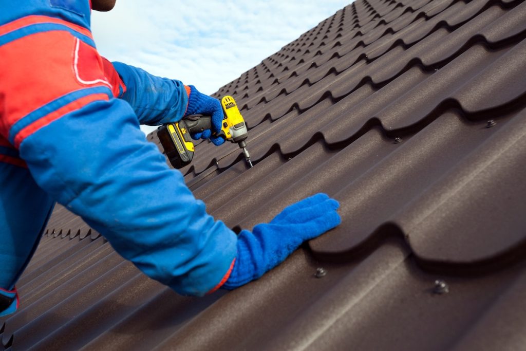 Man worker uses a power drill to attach a cap  metal roofing job with screws.