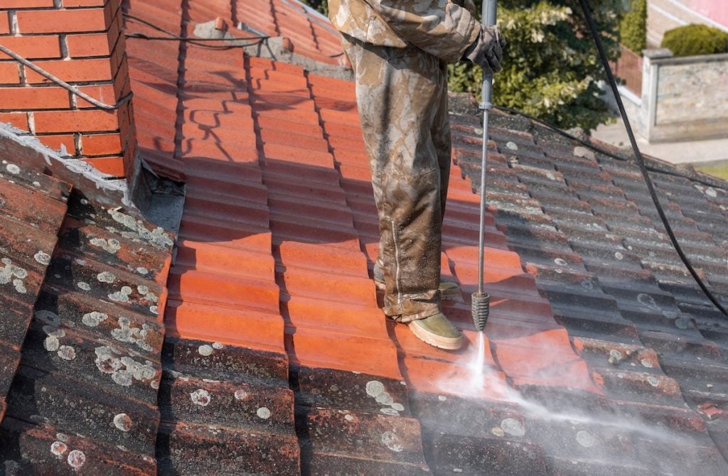 A person in work clothes uses a pressure washer for tile roof 