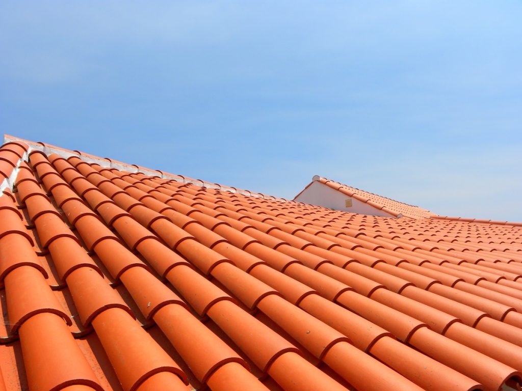 Red tile roof under blue sky. The photo is divided in half. One part is a roof made of clay tiles and the other is a pure blue sky.