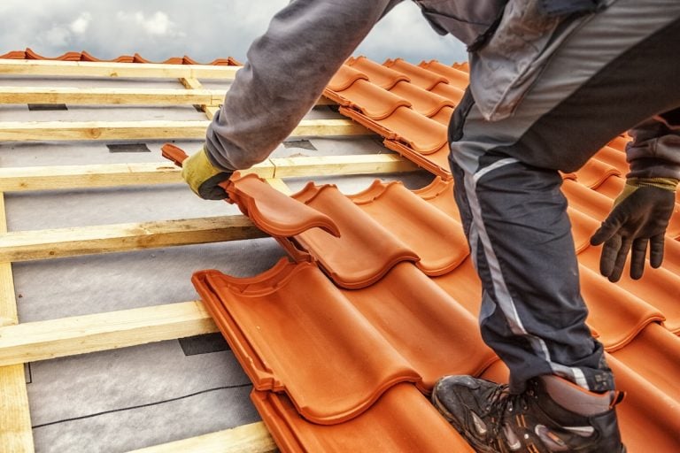 A worker in gloves and workwear performs a tile roof replacement