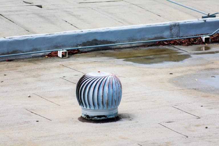 Weathered turbine vent on the flat roof in an industrial building. Ponding water on the settled flat roof.
