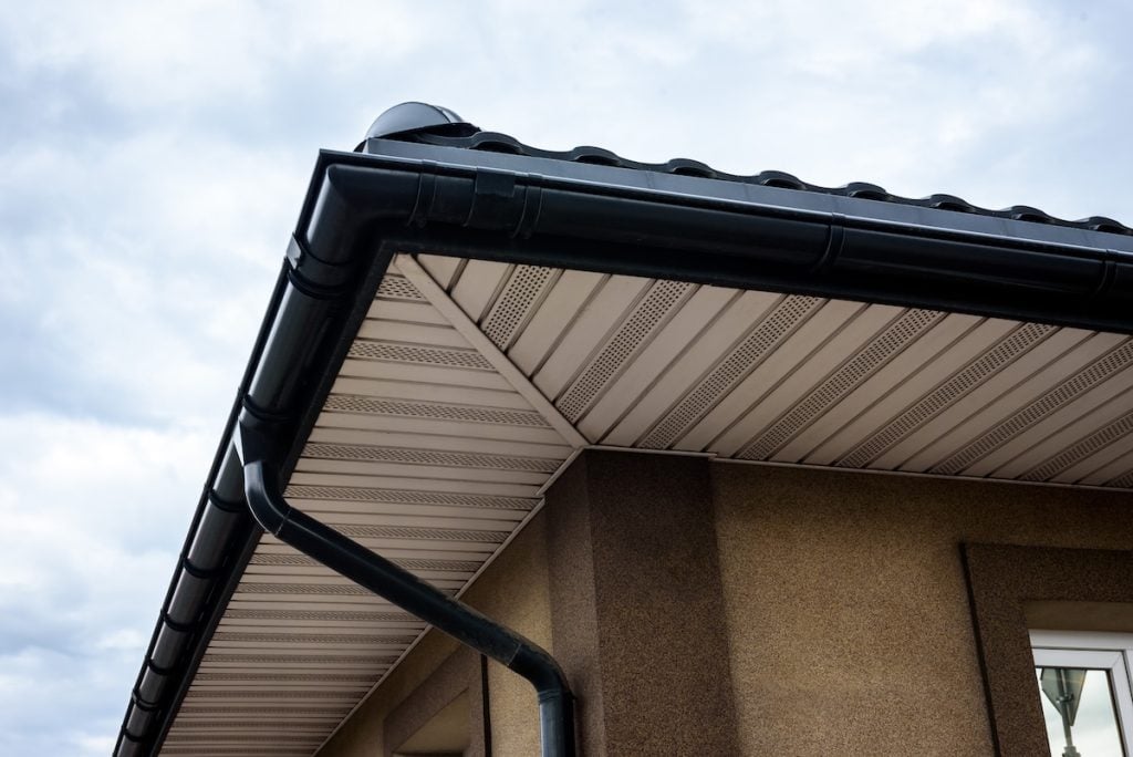 Close-up of a house roof corner showcasing black gutters and downspout