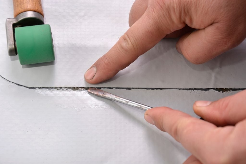 Close-up of hands working with a screwdriver and pressing along a seam in white material