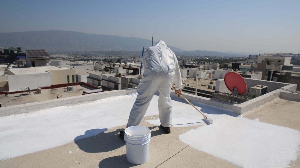 A person in a white protective suit applies commercial roof coatings to a rooftop