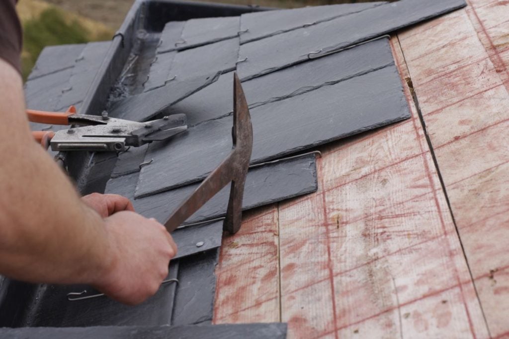 Slate roof repair worker removing shingles with hammer