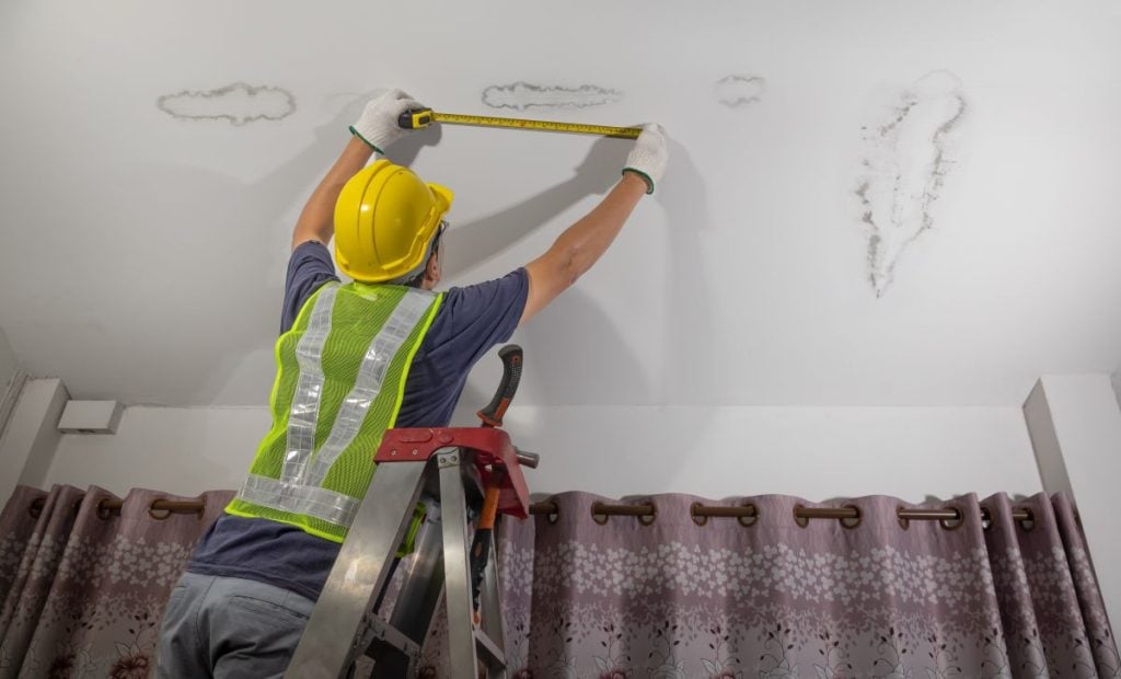 Water stains on ceiling worker using safety helmet measuring stains with meter