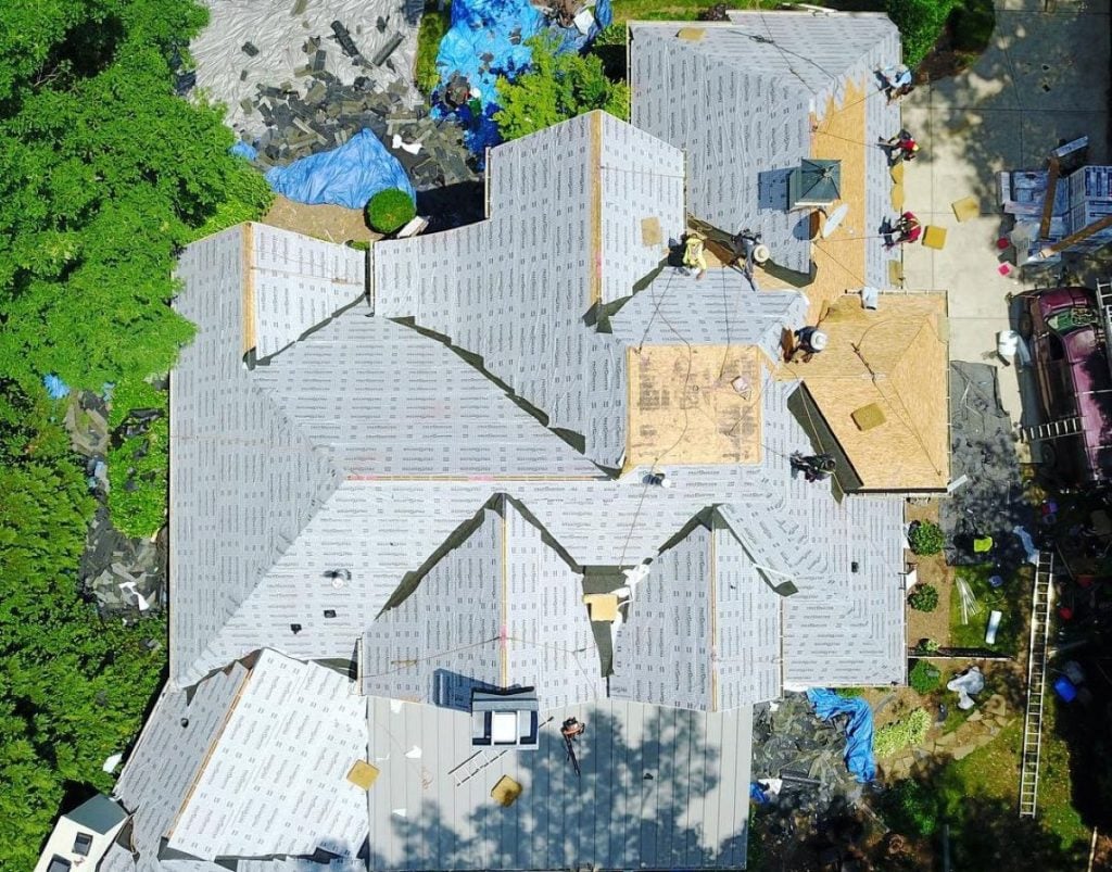 aerial view roof repair vs replacement Roof Medic project workers on top big large house.