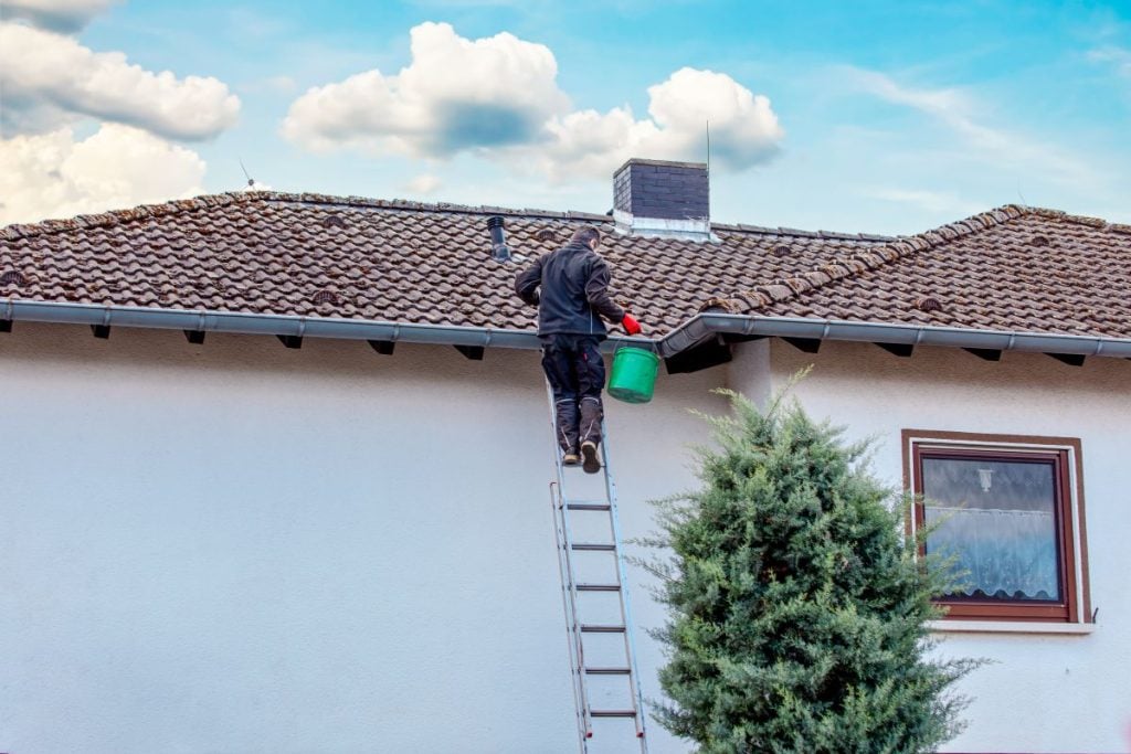 roof debris removal worker on ladder using bucket to remove dirt from gutter
