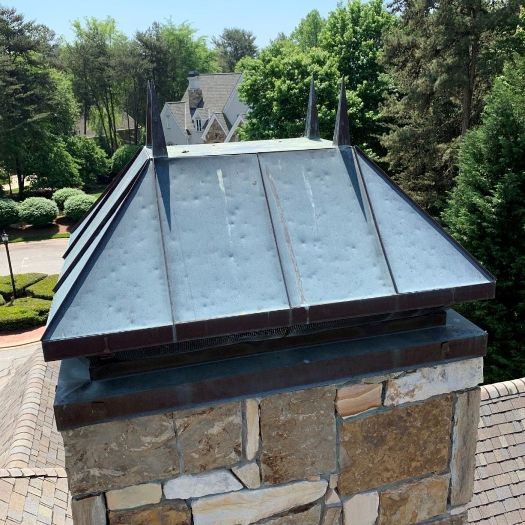 A close-up of a stone chimney with a metal cap showing hail damage