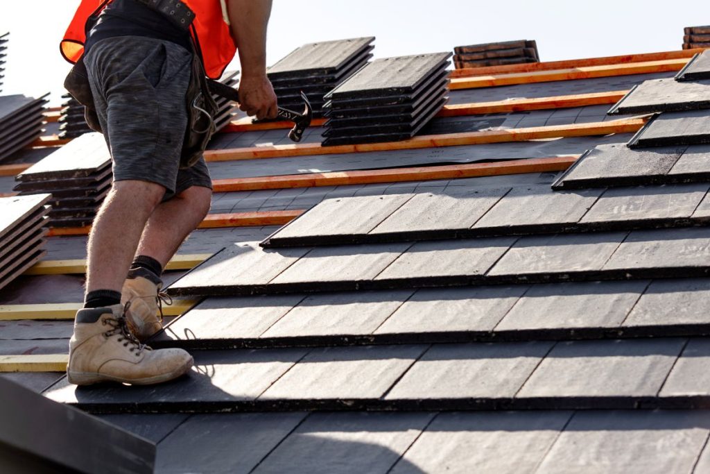 Roofer installs slate roof tiles on a residential building during sunny weather in the afternoon