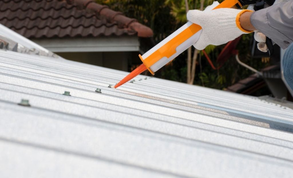 roofer applying metal roof sealant