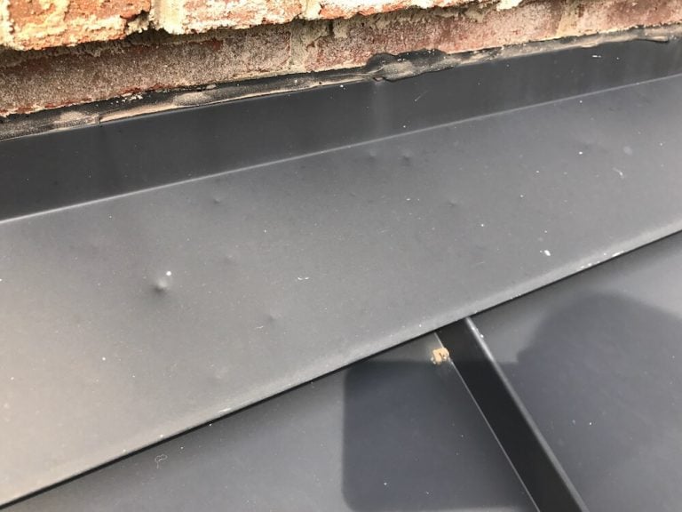 Close-up of a black metal roof with several small dents visible on the surface