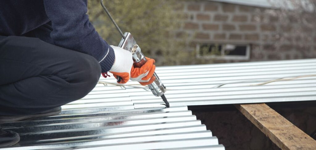 flat roof sealant person wearing gloves uses a sealant gun to apply sealant between metal roofing sheets during installation.