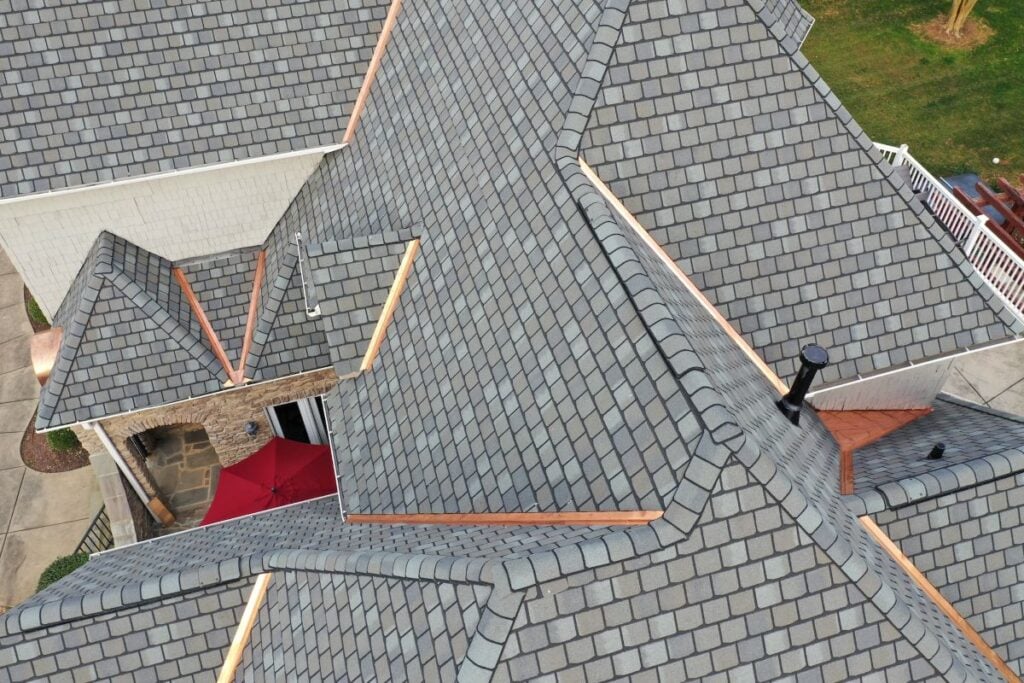 how long do tile roofs last asphalt shingles roof Aerial view of a house roof with gray shingles, intersecting rooflines, and copper flashing. A red umbrella and patio are visible near the bottom left, with a grassy area in the top right.