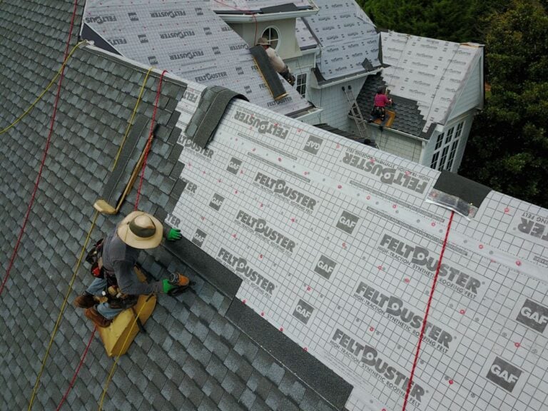 best time to replace a roof Several workers are installing shingles and roofing underlayment on a multi-level house roof. Some rooftops are covered with gray shingles, while others have white underlayment labeled "FELT BUSTER" and "GAF".