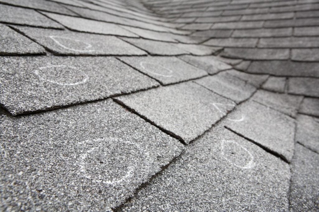 Close-up of asphalt roof shingles with several white chalk circles marking areas, possibly indicating spots of damage or inspection points on the rooftop.