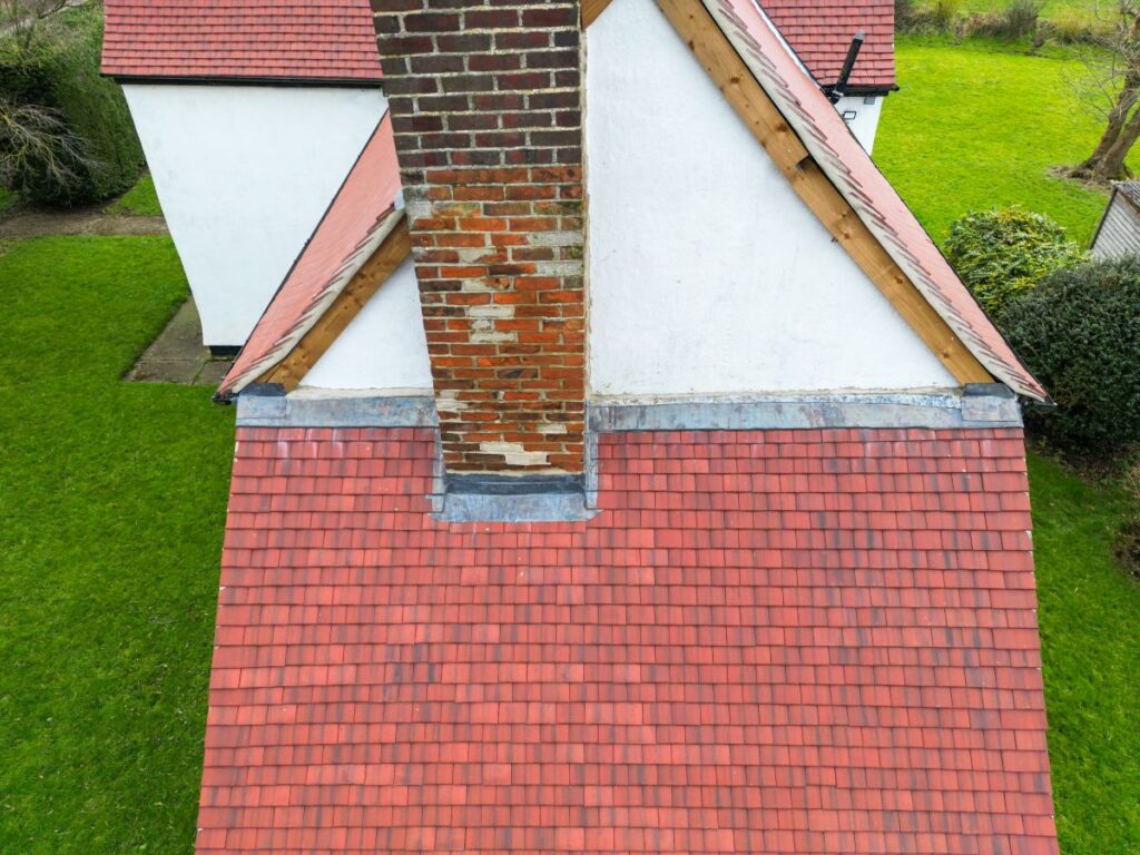 roof to wall flashing detail Aerial view of a red-tiled roof with a brick chimney, white walls, wooden beams, and green grass surrounding the house highlights the roof to wall flashing detail for added protection.